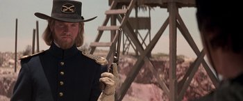Movie still from “The Mask of Zorro” (1998), directed by Martin Campbell – A man holding a gun while standing in front of a wooden structure; Close Up shot, Low angle