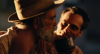Movie still from “The Master” (2012), directed by Paul Thomas Anderson – A man with a beard drinking a cup of coffee while another man looks on; Close Up shot, Over the shoulder angle