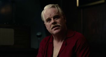 Movie still from “The Master” (2012), directed by Paul Thomas Anderson – A man in a red shirt is sitting in a dark room; Close Up shot, Over the shoulder angle