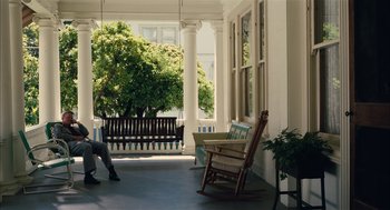 Movie still from “The Master” (2012), directed by Paul Thomas Anderson – A person sitting in a rocking chair on a porch; Wide shot, Low angle