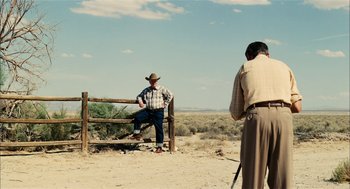 Movie still from “The Master” (2012), directed by Paul Thomas Anderson – A man sitting on top of a wooden fence; Wide shot, Over the shoulder angle