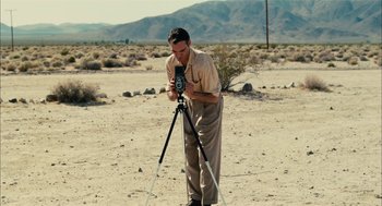 Movie still from “The Master” (2012), directed by Paul Thomas Anderson – A man taking a picture with a camera on a tripod; Wide shot, High angle