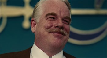 Movie still from “The Master” (2012), directed by Paul Thomas Anderson – An older man with a mustache smiling for the camera; Close Up shot, Over the shoulder angle