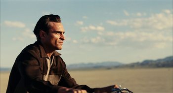 Movie still from “The Master” (2012), directed by Paul Thomas Anderson – A man sitting on a motorcycle in the desert; Close Up shot, Low angle