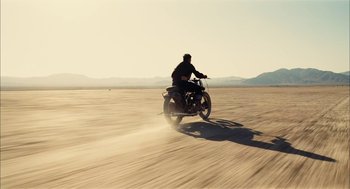 Movie still from “The Master” (2012), directed by Paul Thomas Anderson – A man riding a motorcycle down a dirt road; Extreme Wide shot, Low angle