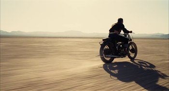 Movie still from “The Master” (2012), directed by Paul Thomas Anderson – A man riding a motorcycle down the middle of a road; Wide shot, Low angle
