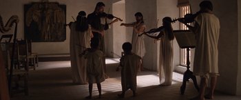 Movie still from “The Mission” (1986), directed by Roland Joffé – A group of people playing musical instruments in a room; Wide shot, Low angle