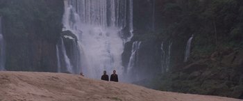 Movie still from “The Mission” (1986), directed by Roland Joffé – Three people are standing on a sand dune near a waterfall; Extreme Wide shot, High angle