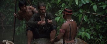 Movie still from “The Mission” (1986), directed by Roland Joffé – A man sitting on the ground next to another man; Wide shot, Low angle