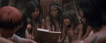 Movie still from “The Mission” (1986), directed by Roland Joffé – A group of people sitting next to each other reading a book; Medium shot, High angle
