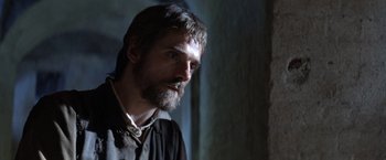 Movie still from “The Mission” (1986), directed by Roland Joffé – A man with long hair and a beard is looking at the camera; Close Up shot, Over the shoulder angle