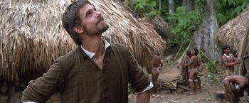 Movie still from “The Mission” (1986), directed by Roland Joffé – A man standing in front of a thatched hut; Medium shot, Over the shoulder angle