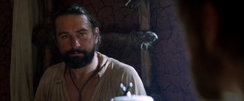 Movie still from “The Mission” (1986), directed by Roland Joffé – A man with a long beard is standing in front of a cross; Close Up shot, Low angle