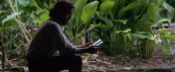 Movie still from “The Mission” (1986), directed by Roland Joffé – A man sitting on the ground reading a book; Medium shot, Low angle