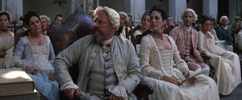 Movie still from “The Mission” (1986), directed by Roland Joffé – A group of people sitting in a row wearing historical clothing; Medium shot, Low angle