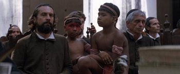 Movie still from “The Mission” (1986), directed by Roland Joffé – A group of young people sitting next to each other; Medium shot, Over the shoulder angle