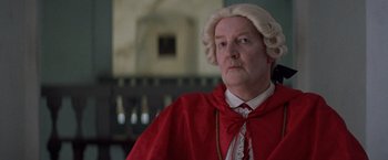 Movie still from “The Mission” (1986), directed by Roland Joffé – An older man in a wig and a red cape; Close Up shot, Low angle