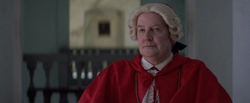 Movie still from “The Mission” (1986), directed by Roland Joffé – An older woman wearing a wig and a red robe; Close Up shot, Low angle