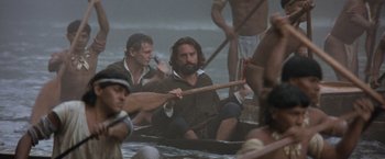 Movie still from “The Mission” (1986), directed by Roland Joffé – A group of people rowing a boat in the water; Medium shot, Over the shoulder angle