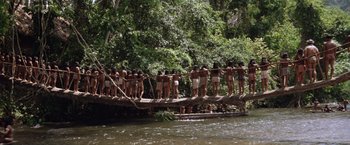Movie still from “The Mission” (1986), directed by Roland Joffé – A group of people standing on top of a wooden bridge over a river; Extreme Wide shot, High angle