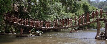 Movie still from “The Mission” (1986), directed by Roland Joffé – A group of people standing on top of a wooden bridge over a river; Extreme Wide shot, High angle