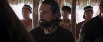 Movie still from “The Mission” (1986), directed by Roland Joffé – A man with long hair and a beard is looking at the camera; Close Up shot, Over the shoulder angle