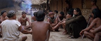 Movie still from “The Mission” (1986), directed by Roland Joffé – A group of people sitting on the ground in front of a building; Wide shot, High angle