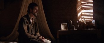 Movie still from “The Mission” (1986), directed by Roland Joffé – A man sitting on a chair in front of a table; Wide shot, Over the shoulder angle