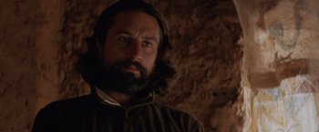 Movie still from “The Mission” (1986), directed by Roland Joffé – A man with long hair and a beard is looking at the camera; Close Up shot, Over the shoulder angle