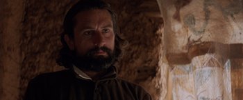 Movie still from “The Mission” (1986), directed by Roland Joffé – A man with long hair and a beard is looking at the camera; Close Up shot, Low angle