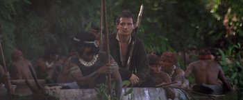 Movie still from “The Mission” (1986), directed by Roland Joffé – A group of people sitting in the woods holding arrows; Medium shot, Low angle
