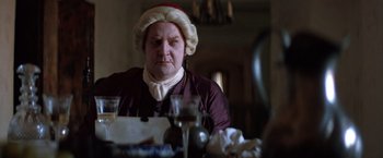 Movie still from “The Mission” (1986), directed by Roland Joffé – An old man wearing a hat sitting at a dinner table; Close Up shot, Over the shoulder angle