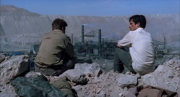 Movie still from “The Motorcycle Diaries” (2004), directed by Walter Salles – Two men sitting on the ground in front of an industrial area; Wide shot, High angle