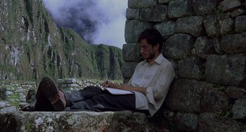 Movie still from “The Motorcycle Diaries” (2004), directed by Walter Salles – A man sitting on a stone wall writing on a notebook; Medium shot, Low angle
