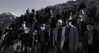 Movie still from “The Motorcycle Diaries” (2004), directed by Walter Salles – A group of men standing next to each other in front of a rock wall; Wide shot, Low angle