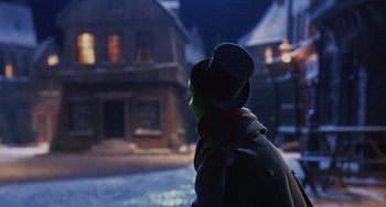 Movie still from “The Muppet Christmas Carol” (1992), directed by Brian Henson – A person wearing a hat standing in front of a building; Close Up shot, Over the shoulder angle