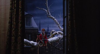 Movie still from “The Muppet Christmas Carol” (1992), directed by Brian Henson – A person in a red coat and a red hat is standing on a tree branch; Wide shot, High angle