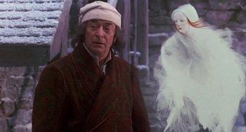 Movie still from “The Muppet Christmas Carol” (1992), directed by Brian Henson – A man wearing a white hat standing in front of an image of a woman; Medium shot, Over the shoulder angle