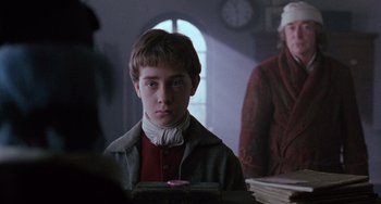 Movie still from “The Muppet Christmas Carol” (1992), directed by Brian Henson – A young boy is looking at the camera while a woman watches; Close Up shot, Over the shoulder angle