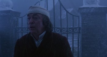 Movie still from “The Muppet Christmas Carol” (1992), directed by Brian Henson – An older man wearing a white hat standing in front of a gate; Close Up shot, Over the shoulder angle