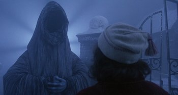 Movie still from “The Muppet Christmas Carol” (1992), directed by Brian Henson – A person in a hooded cloak standing in front of a statue; Medium shot, Over the shoulder angle