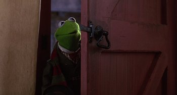 Movie still from “The Muppet Christmas Carol” (1992), directed by Brian Henson – A kermit the frog puppet looking through a door knob; Medium shot, Low angle