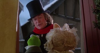 Movie still from “The Muppet Christmas Carol” (1992), directed by Brian Henson – A person wearing a top hat and holding a stuffed animal; Medium shot, Over the shoulder angle