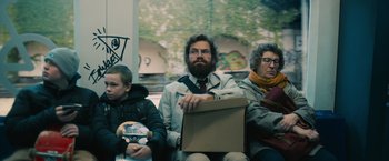 Movie still from “Riders of Justice” (2020), directed by Anders Thomas Jensen – A man sitting on a train with a box in his lap; Medium shot, Over the shoulder angle