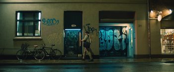Movie still from “Riders of Justice” (2020), directed by Anders Thomas Jensen – A man walking down the street in front of a building; Wide shot, Over the shoulder angle