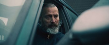Movie still from “Riders of Justice” (2020), directed by Anders Thomas Jensen – A man with a gray beard sitting in the driver's seat of a car; Close Up shot, Over the shoulder angle