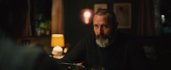 Movie still from “Riders of Justice” (2020), directed by Anders Thomas Jensen – A man sitting at a table in a dark room; Close Up shot, Over the shoulder angle