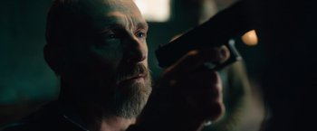 Movie still from “Riders of Justice” (2020), directed by Anders Thomas Jensen – A man with a beard holding a gun in a dark room; Close Up shot, Low angle