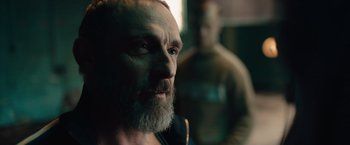 Movie still from “Riders of Justice” (2020), directed by Anders Thomas Jensen – A man with a goatee is looking into the distance; Close Up shot, Over the shoulder angle