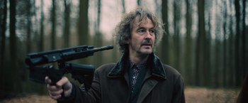 Movie still from “Riders of Justice” (2020), directed by Anders Thomas Jensen – A man holding a rifle in a forest; Medium shot, Low angle